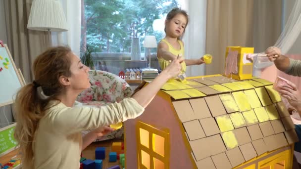 Νεαρή οικογένεια με παιδί κτίριο και Ζωγραφική παιχνίδι χαρτόνι σπίτι μαζί. — Αρχείο Βίντεο