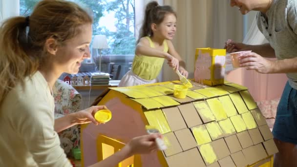 Familia joven con construcción de niños y pintar casa de cartón de juguete juntos . — Vídeos de Stock