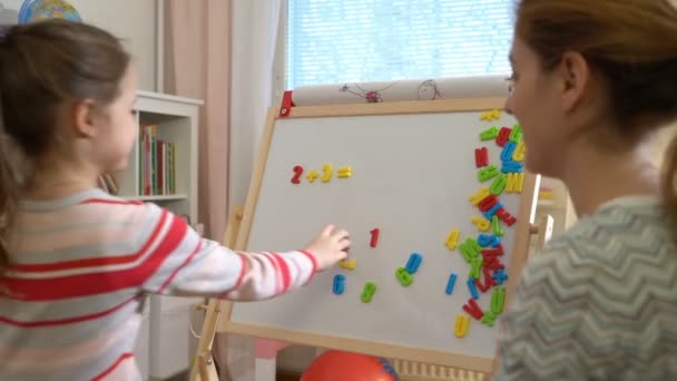 Молодая мать объясняет арифметику милой маленькой дочери дома — стоковое видео