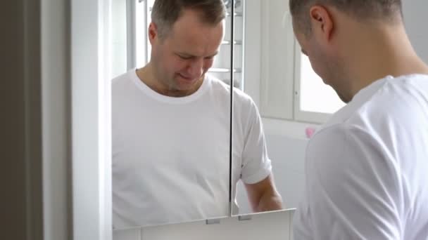 Un homme avec un gant en caoutchouc nettoie un lavabo dans la salle de bain et sourit à la caméra — Video