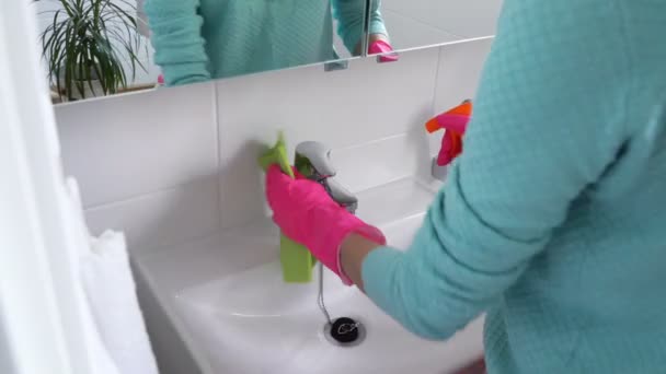 Жінка з гумовою рукавичкою очищає раковину у ванній кімнаті і посміхається на камеру — стокове відео