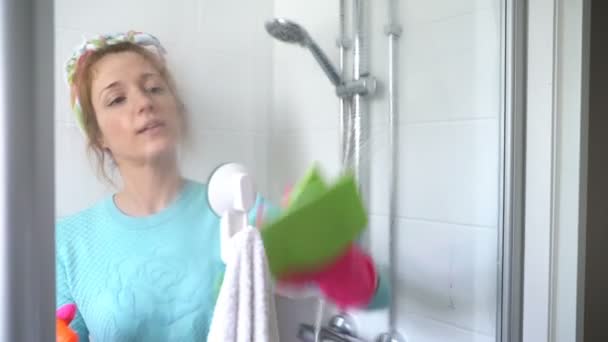 Woman with a rubber glove cleans a shower stall and smiles at the camera — Stock Video