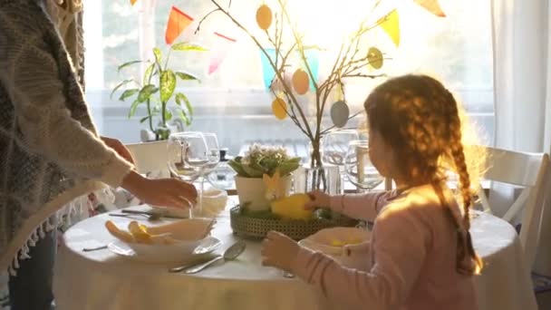 女性と彼女の小さな娘がウサギと卵の装飾とイースターお祝いテーブルを設定します。 — ストック動画