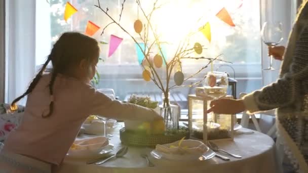 Woman and her little daughter are setting easter festive table with bunny and eggs decoration — Stock Video