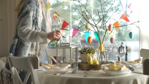 Молодая женщина накрывает пасхальный праздничный стол с украшением из кролика и яиц — стоковое видео