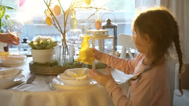 Mujer y su hija pequeña están poniendo la mesa festiva de Pascua con conejito y huevos decoración — Vídeos de Stock