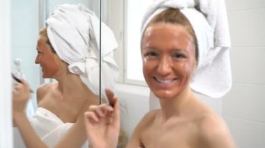 Beyaz bir havlu ile genç bir kadın onun yüzünde kahverengi nemlendirici maske koymak.