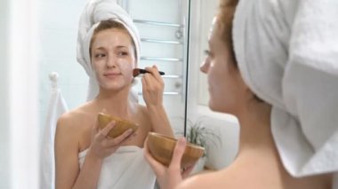 Genç kadın beyaz bir havlu ile onun yüzünde nemlendirici maske koymak.