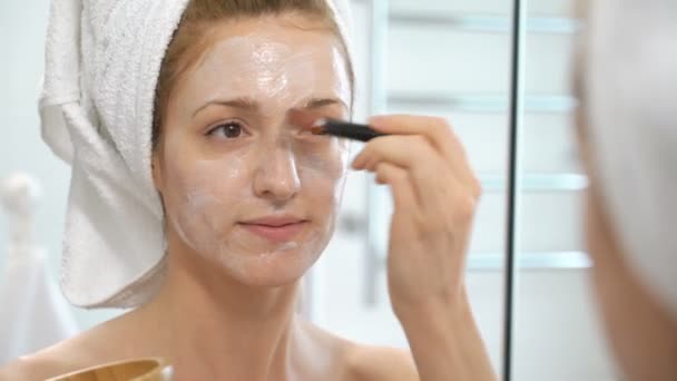 Jonge vrouw met een witte handdoek zetten van haar gezicht een hydraterende masker — Stockvideo