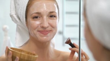 Genç kadın beyaz bir havlu ile onun yüzünde nemlendirici maske koymak.