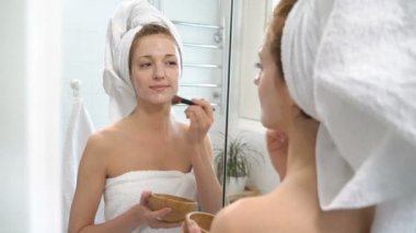 Genç kadın beyaz bir havlu ile onun yüzünde nemlendirici maske koymak.