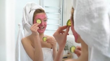 Pembe yüz nemlendirici maske olan kadın salatalık dilimleri ile çalış