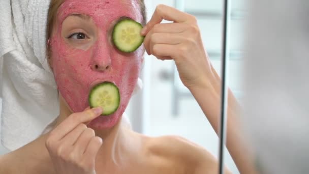 Jovem com uma máscara hidratante facial rosa brinca com fatias de pepino — Vídeo de Stock