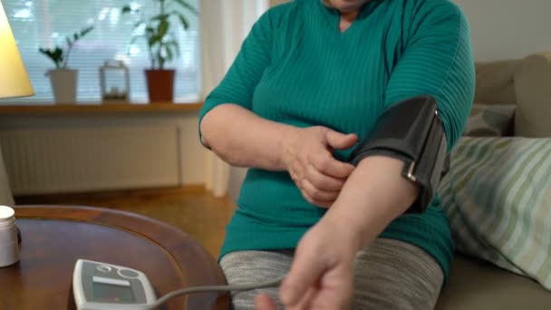 Eine ältere Frau misst den Blutdruck und nimmt Tabletten zu Hause ein. — Stockvideo