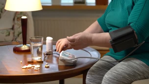 Літня жінка вимірює кров'яний тиск і приймає таблетки вдома . — стокове відео