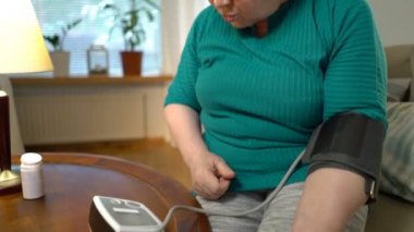 Yaşlı bir kadın tansiyon ölçer ve evde hap alır.