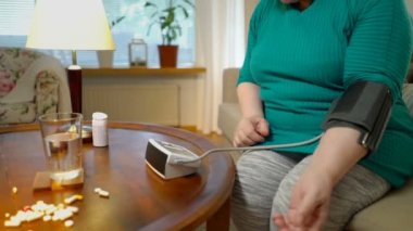 Yaşlı bir kadın tansiyon ölçer ve evde hap alır.