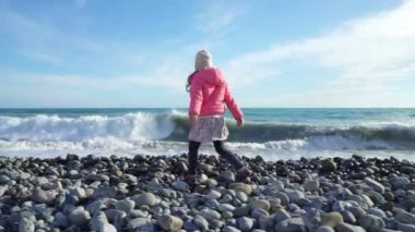 Soğuk bahar gününde dalgalar deniz kenarında oynamaktan pembe ceket sevimli küçük kız