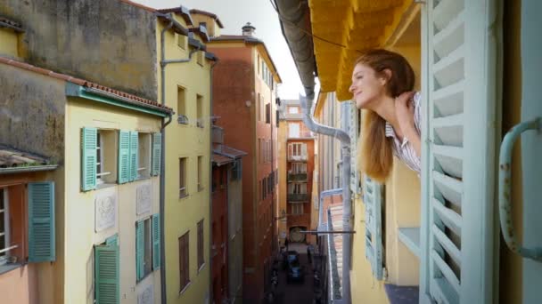 A young woman looking out of the window to a medieval street smiling and waving her hand — Stock Video