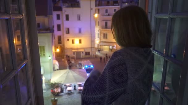 Ночной инцидент в городе. Машина скорой помощи на улице. Возбужденная молодая женщина смотрит в окно своего дома . — стоковое видео