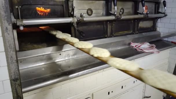 Traditionele Italiaanse bakkerij. De vrouw Baker zet het brood in de oven voor het bakken met behulp van een speciale lange boord. — Stockvideo