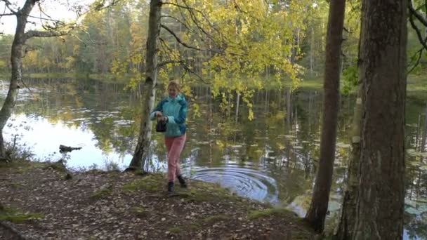 Una mujer joven saca agua de un lago del bosque y hace café en un fuego abierto . — Vídeos de Stock