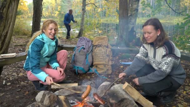 Młode kobiety smażą kiełbaski na otwartym ogniu w lesie — Wideo stockowe