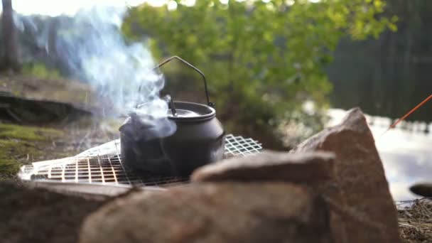Chaleira tee koffee em uma churrasqueira descartável abrir fogo com panela moka na margem de um lago florestal — Vídeo de Stock