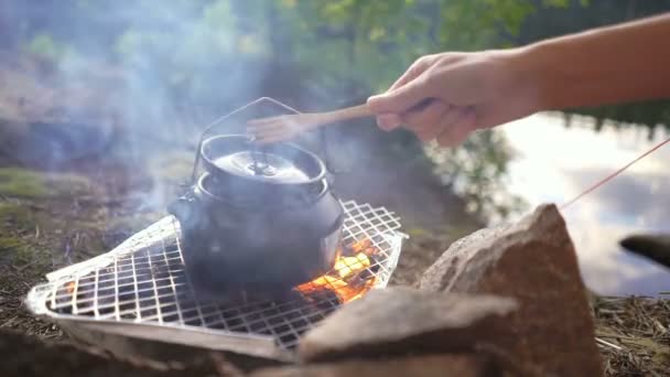 Tee koffee bouilloire sur un barbecue jetable feu ouvert avec pot de moka sur le rivage d'un lac forestier — Video