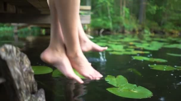 Jovem casal desfrutando de silêncio junto ao lago da floresta sentado à beira de um molhe de madeira — Vídeo de Stock
