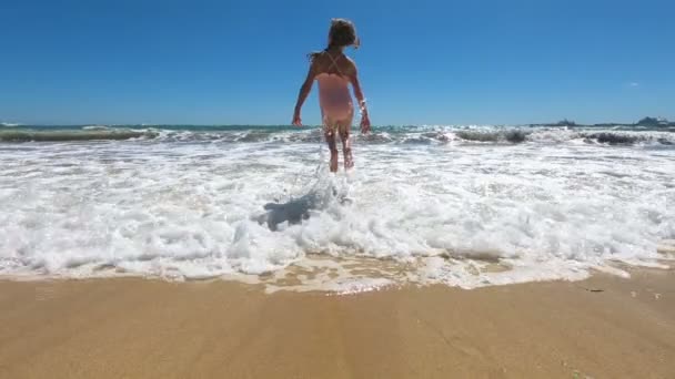 Glad liten flicka bär rosa baddräkt hoppa och leka med se vågor på stranden — Stockvideo