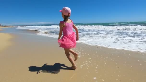 Plajda çıplak ayakla koşan pembe mayo giymiş küçük bir kız. — Stok video
