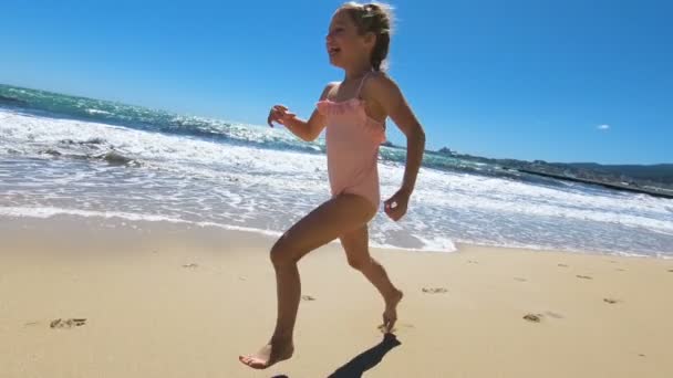 Маленька дівчинка в рожевому купальнику біжить на пляжі босоніж — стокове відео