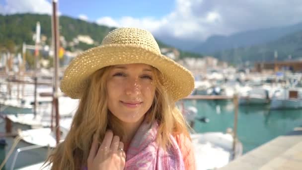 Portrait of young woman wearing straw hat smiling at the camera with seacoast background. — Stock Video