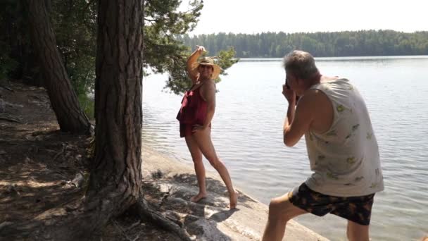 Пожилой мужчина фотографирует привлекательную пожилую женщину с винтажной камерой на пляже . — стоковое видео