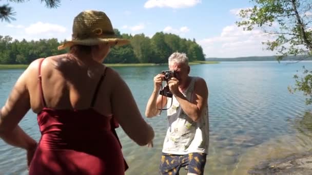 Älterer Mann fotografiert attraktive Seniorin mit Oldtimer-Kamera am Strand. — Stockvideo