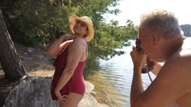 Älterer Mann fotografiert attraktive Seniorin mit Oldtimer-Kamera am Strand. — Stockvideo