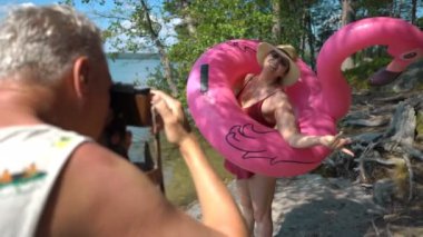 Yaşlı bir adam sahilde eski model fotoğraf makinesiyle çekici yaşlı bir kadının fotoğrafını çekiyor..