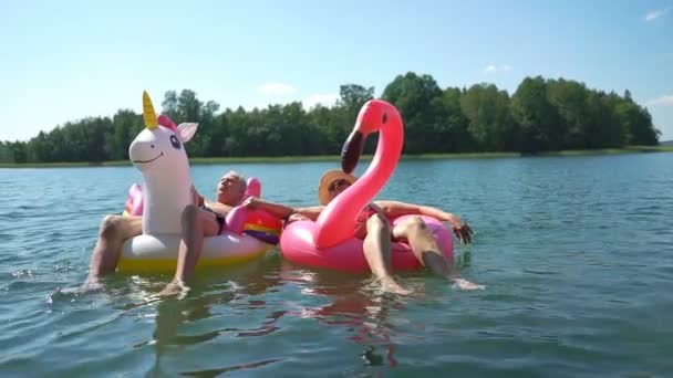 Älteres Paar schwimmt auf aufblasbarem Flamingo und Einhorn. — Stockvideo