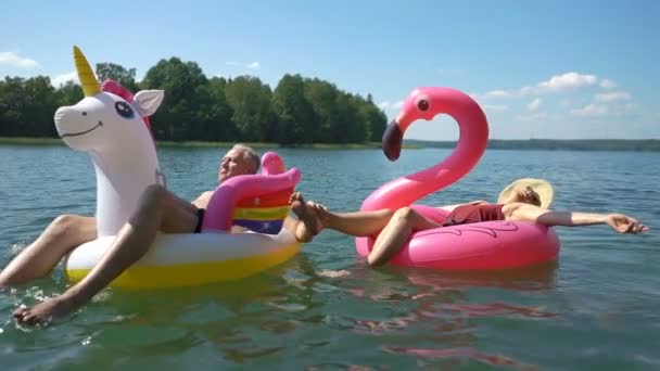 Starsza para pływająca na nadmuchiwanym flamingu i jednorożcu. — Wideo stockowe