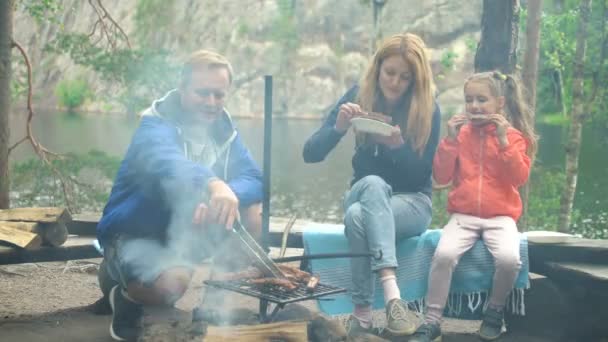 Ein Paar mit Kind grillt im Wald am Ufer des Sees — Stockvideo