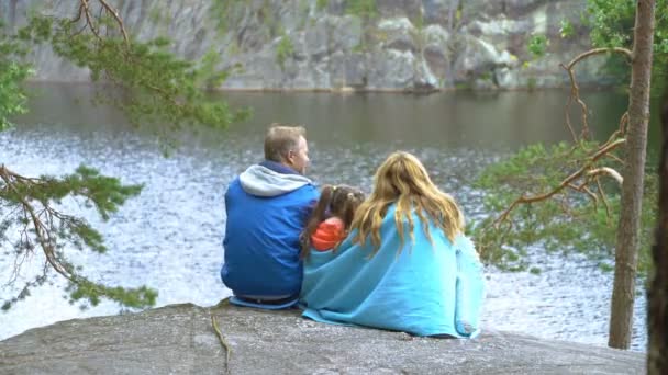 Gezin met kind zittend op de rotsachtige oever van een bos meer — Stockvideo