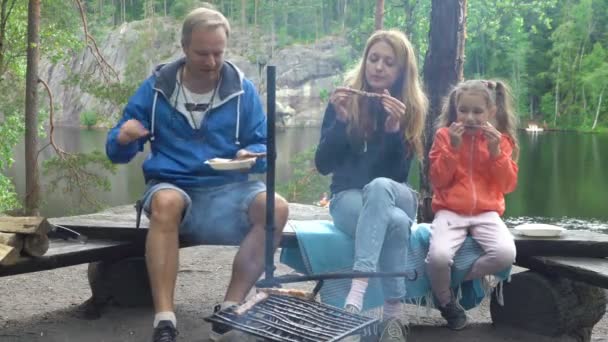 Una pareja con un niño a la parrilla en el bosque a orillas del lago — Vídeos de Stock