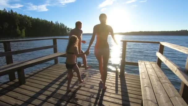 Para rodzinna z córką biegającą po drewnianym molo i skaczącą do jeziora — Wideo stockowe