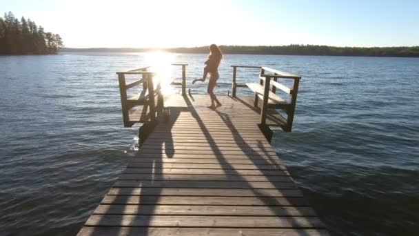 Una joven esbelta con su hija jugando en un muelle de madera junto al lago — Vídeos de Stock