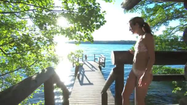 Uma mulher correndo pelas escadas da sauna para o cais de madeira para saltar para o lago — Vídeo de Stock