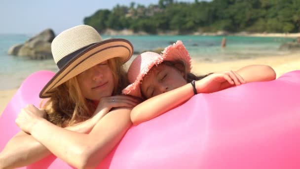 Hasır şapkalı anne ve kızı, pembe şişme koltukta uzanan kumsalda aylaklık etmekten hoşlanırlar. — Stok video