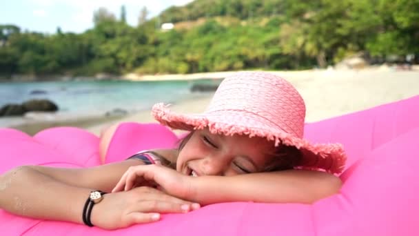 Plajdaki şişme koltukta pembe hasır şapka takan küçük bir kız. — Stok video