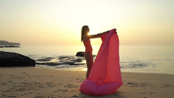 Egy szalmakalapot viselő fiatal nő élvezi a nyugalmat és a magánéletet naplementekor a parton. — Stock videók