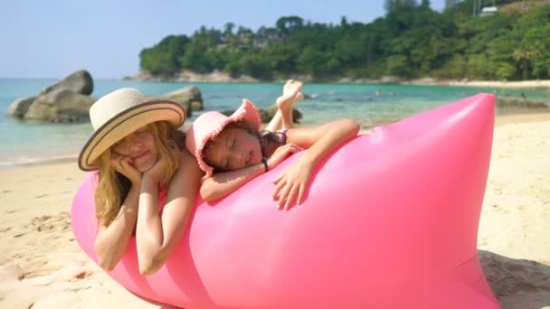 Mamá y su hija en sombreros de paja disfrutan de la ociosidad en una playa acostada en un sofá inflable rosa — Vídeo de stock